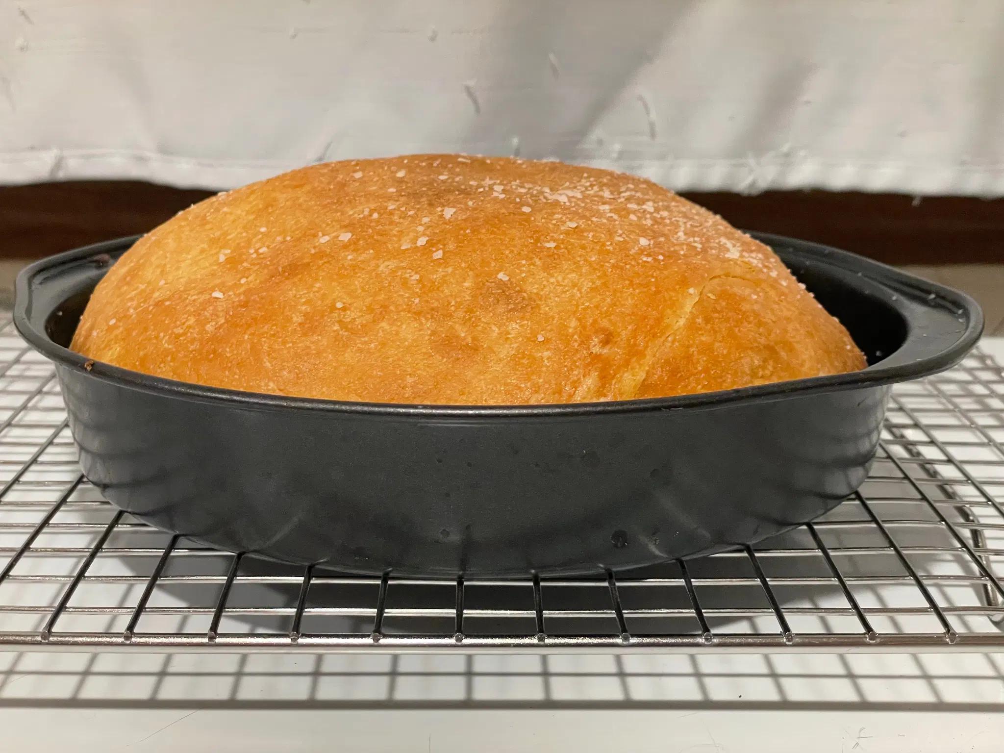 Brown bread in an 8 inch cake tin that it was baked in. Kosher salt is dusted over the top. Shown almost side on to demonstrate its size and shape.